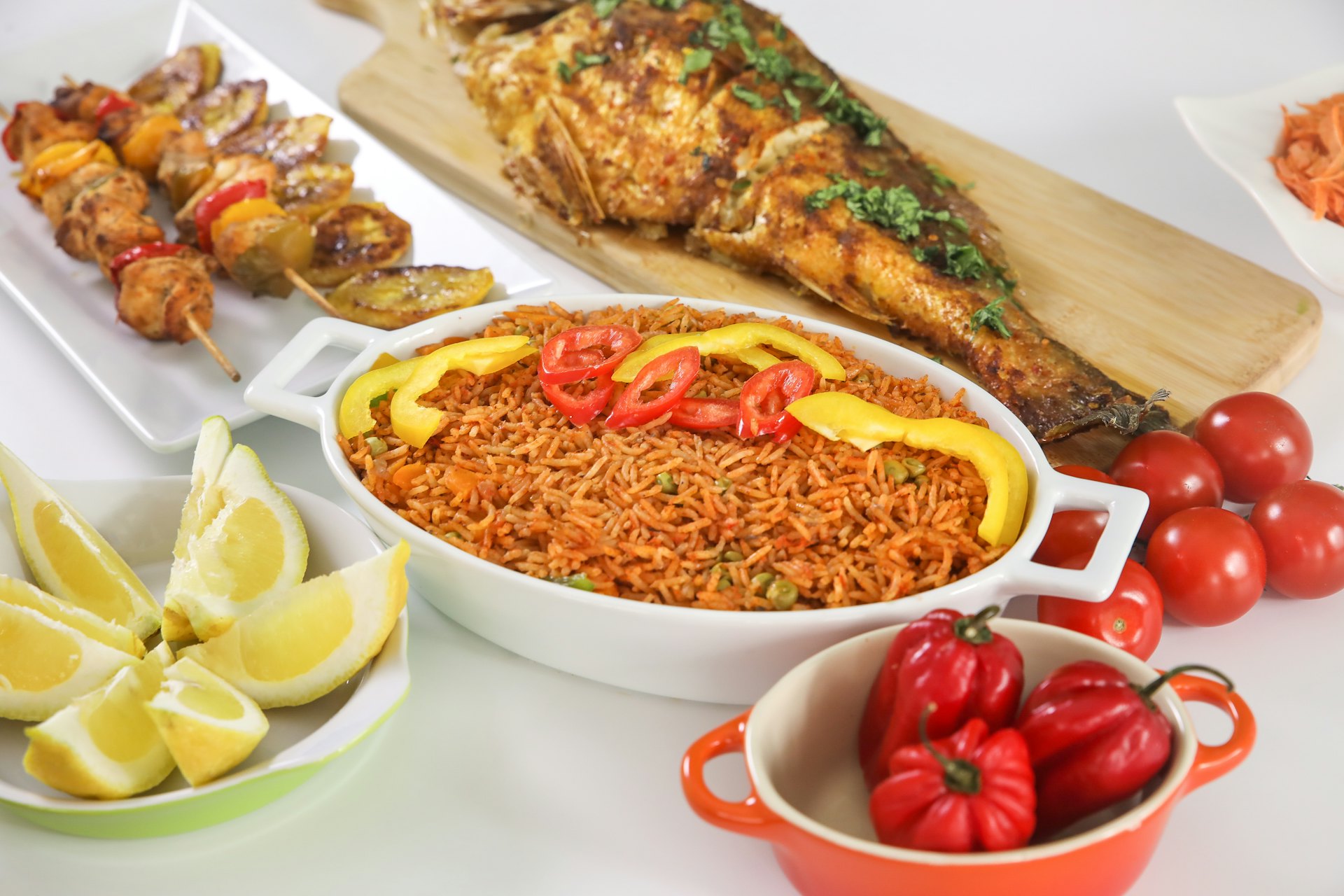 Jollof rice served with grilled fish, chicken skewers and fresh peppers